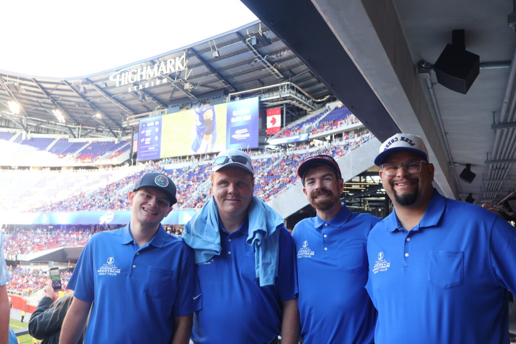 Four attendees in Foundation polo shirts posing in the stands