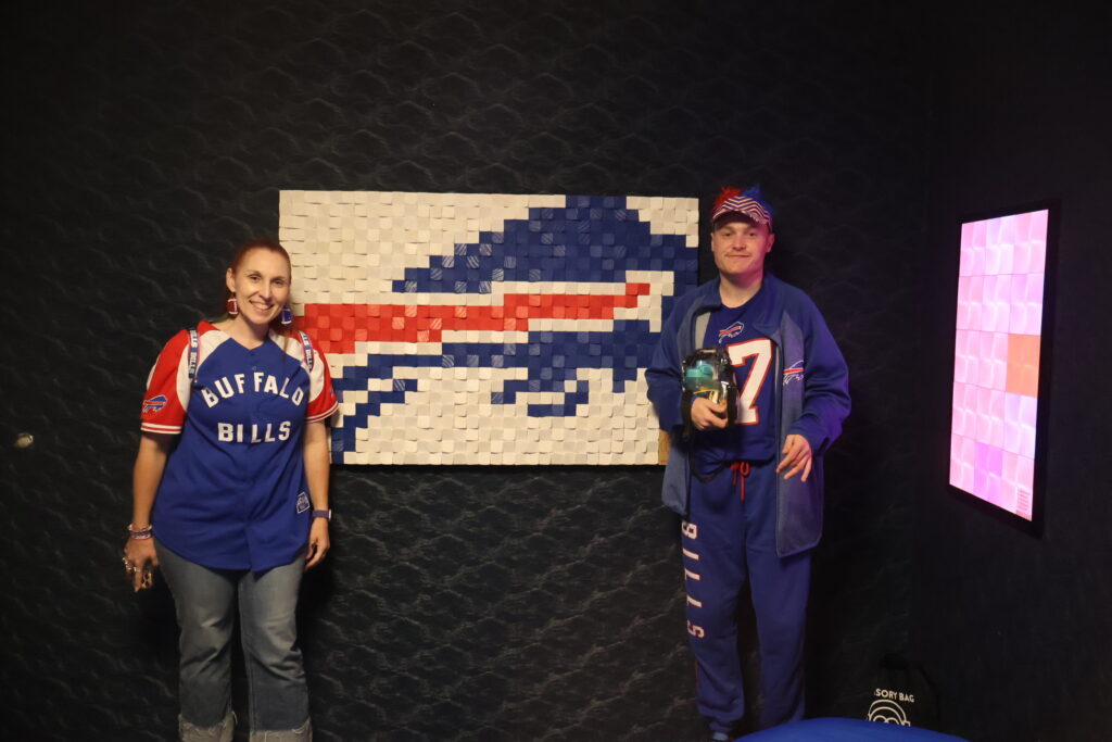 Two attendees beside a tactile Buffalo Bills logo mosaic in the sensory room