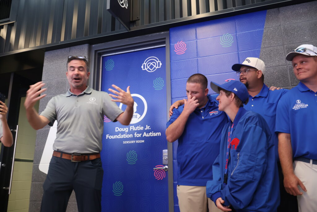 A host speaking beside the Doug Flutie Jr. Foundation for Autism sensory room door
