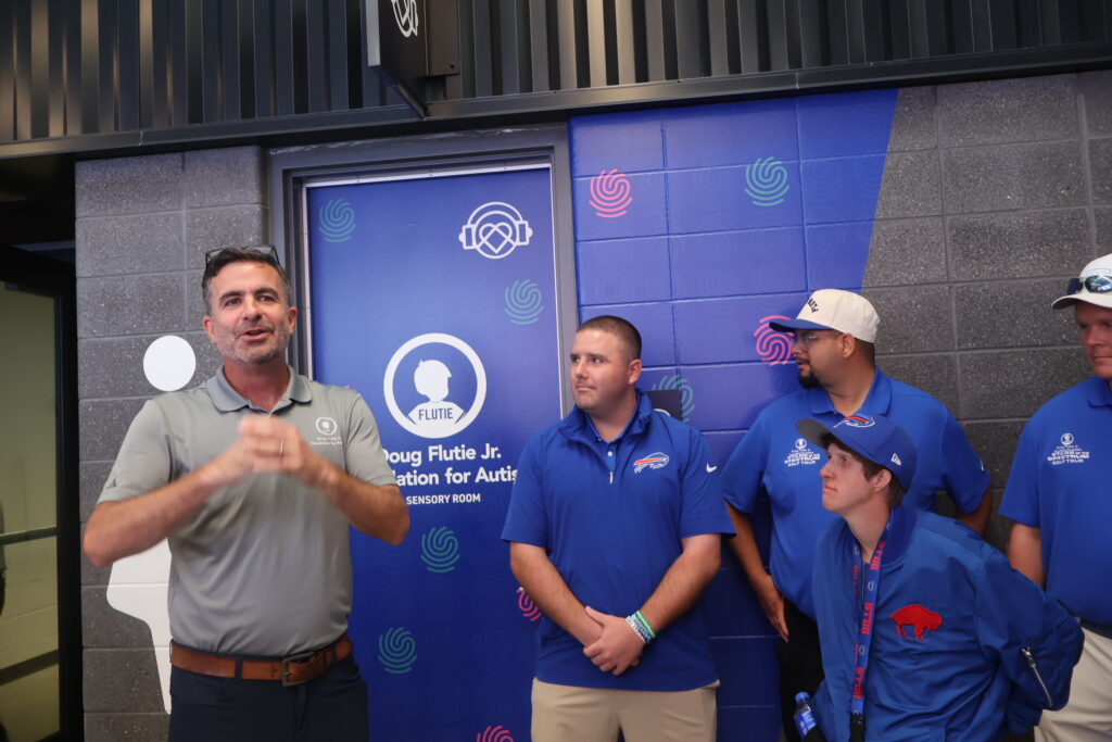 A man addressing a small group in front of the sensory room banner