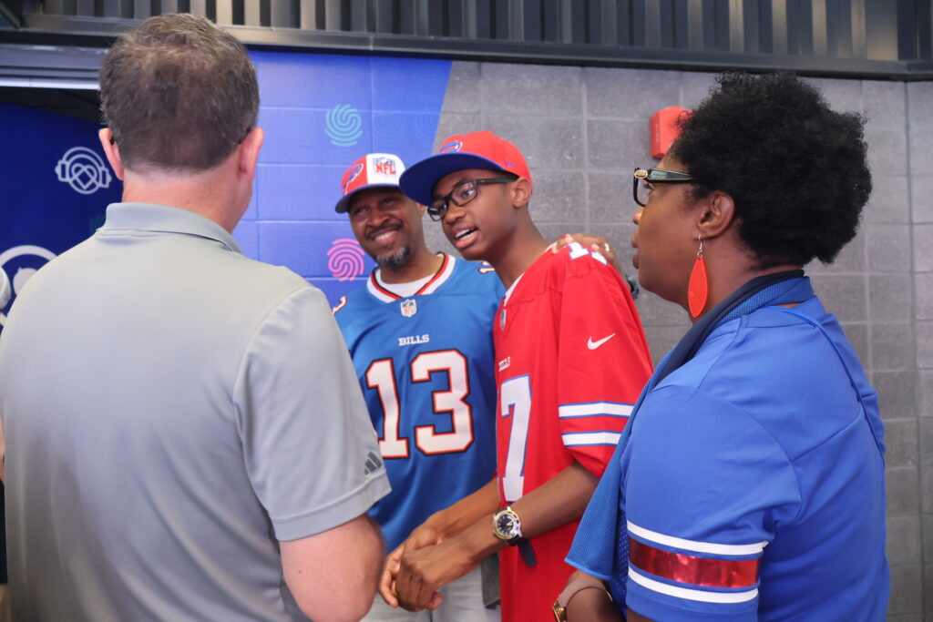 A staff member greets a family wearing Buffalo Bills jerseys and caps outside the sensory room