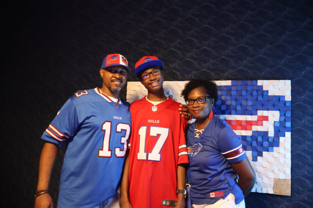 A family of three in Buffalo Bills jerseys posing in front of a Bills wall mural