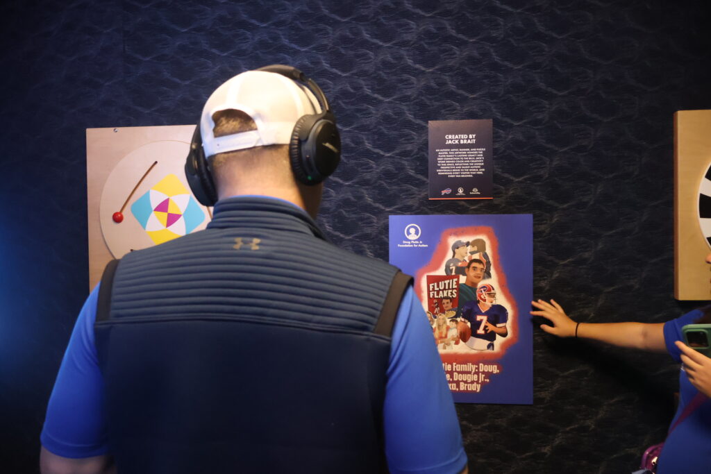 A visitor wearing noise-cancelling headphones reads a Flutie Flakes display panel on the sensory room wall