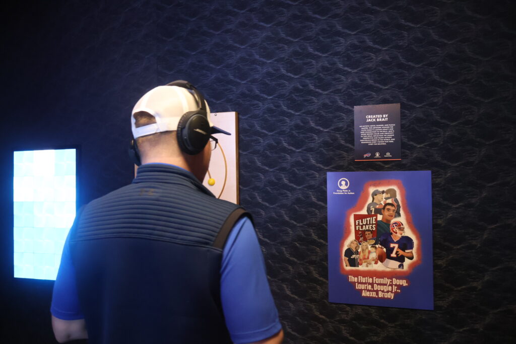 A visitor in noise-cancelling headphones beside a lit sensory panel and a Flutie Flakes poster