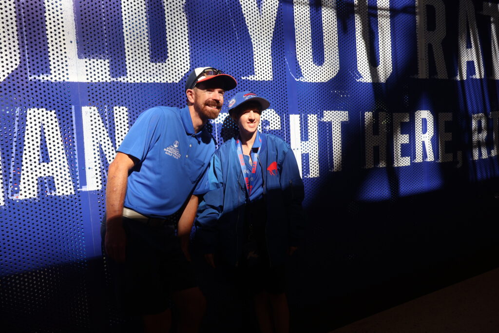 Two people in Foundation polo shirts in front of an illuminated stadium wall graphic