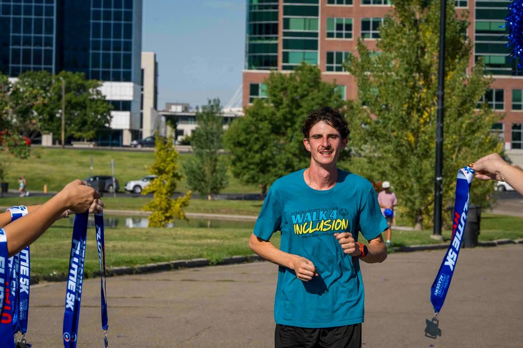A runner reaching the finish as volunteers hold out Flutie 5K medals