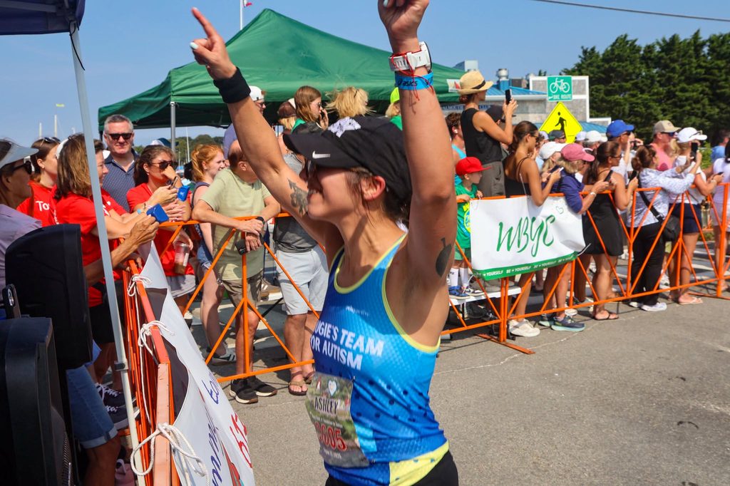 A Dougie's Team for Autism runner raises both arms as she nears the finish, with spectators cheering from behind the barriers