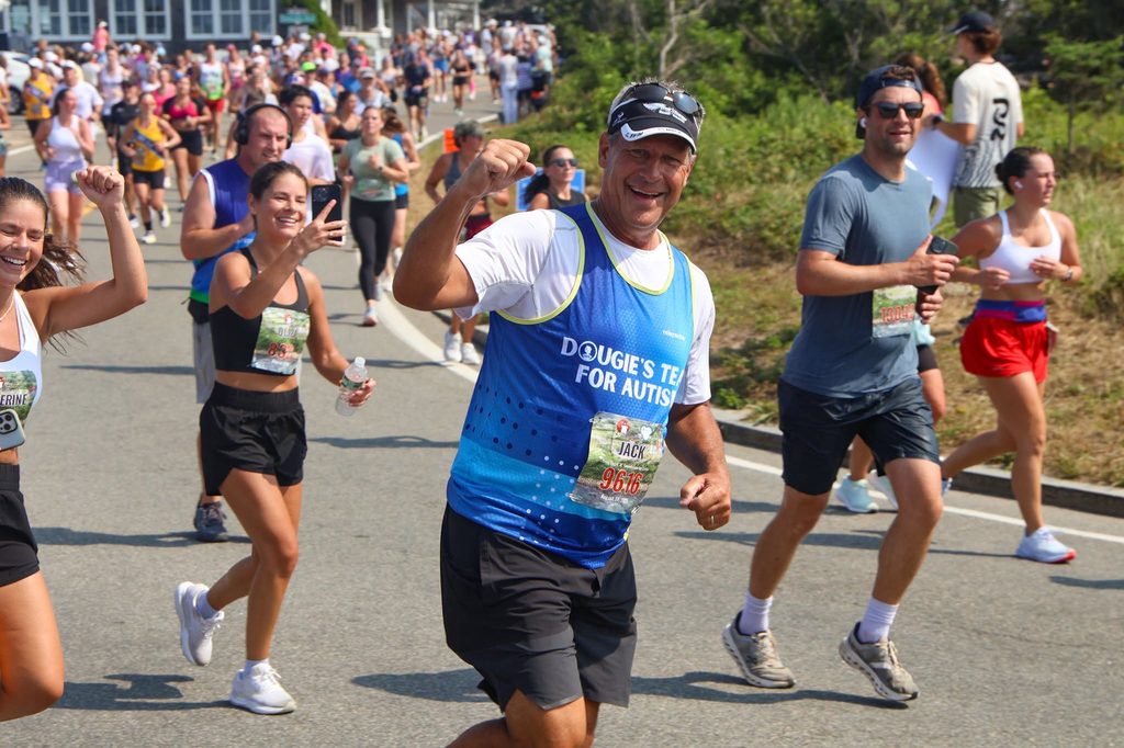 A Dougie's Team for Autism runner in a visor pumps his fist as he passes the crowd