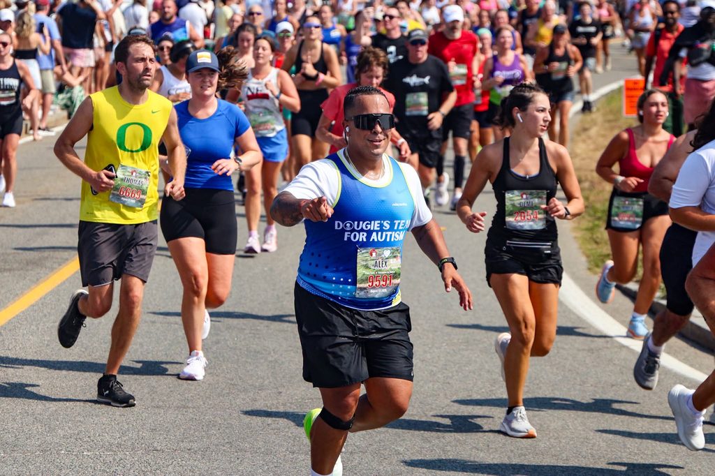 A runner in a Dougie's Team for Autism singlet points toward the camera mid-race