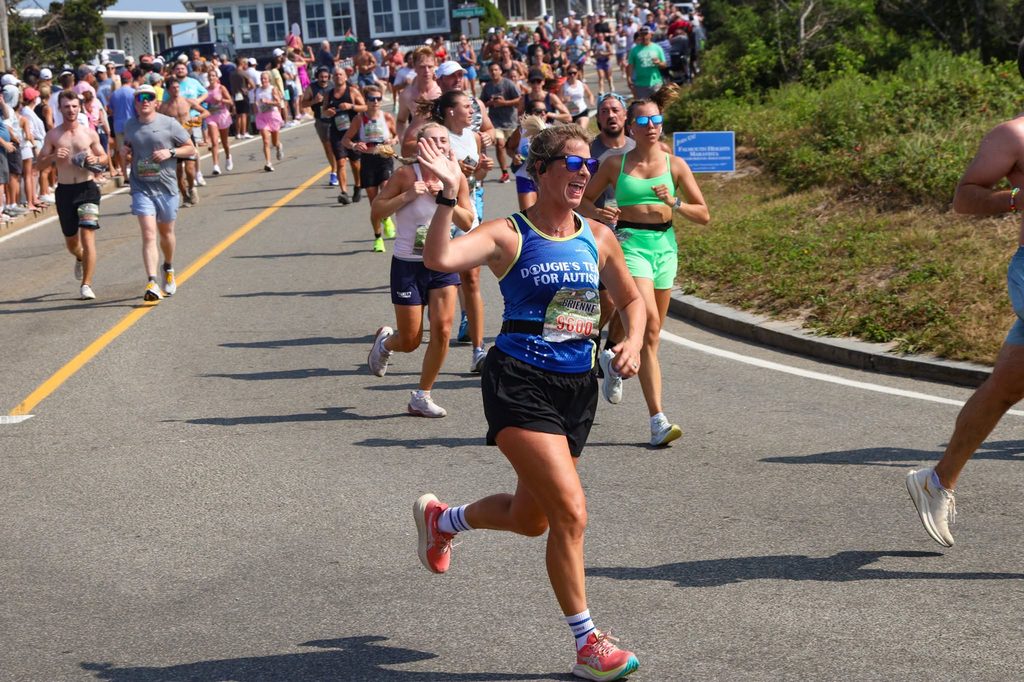 A Dougie's Team for Autism runner waves to spectators on a sunny coastal road