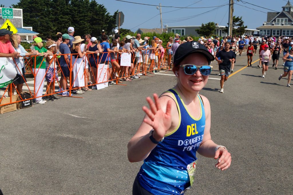 A Dougie's Team for Autism runner waves toward the camera as she passes the crowd barriers