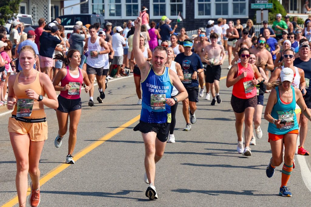 A Dougie's Team for Autism runner raises one finger in the air as he passes the crowd