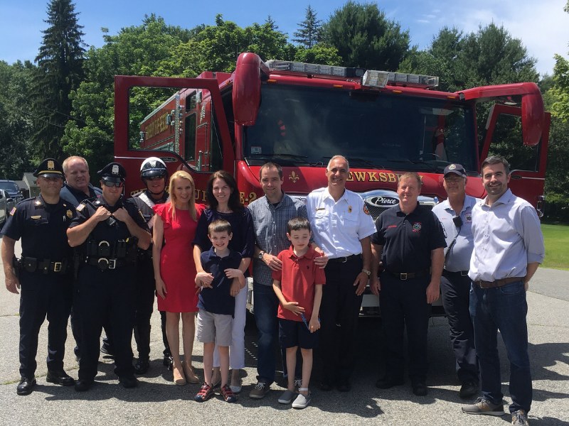Police officers, firefighters, parents and two young children standing together in front of a Tewksbury fire engine